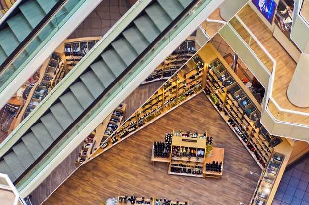 Aerial view of escalators resting a floor above a wine and liquor retail store layout.
