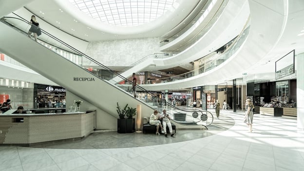 A multi-story shopping center architecture with a circular design ringed with retail shops and two escalators leading to higher floors.