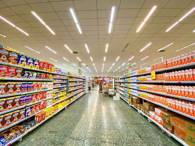 An aisle of a store stretches into the distance, with rows of food items arranged on either side of the camera.